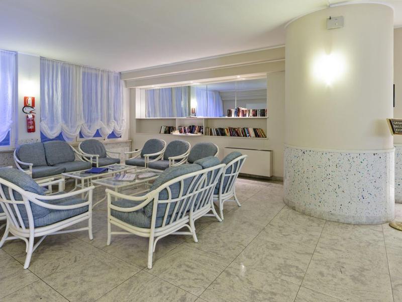 Area d'attesa luminosa con mobili bianchi e cuscini blu in un hotel.