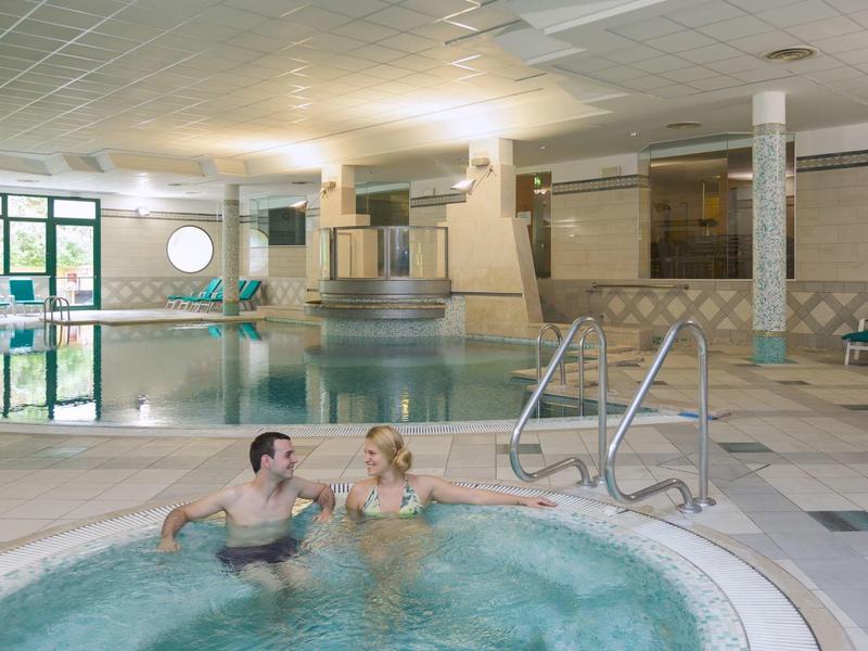 Una coppia si rilassa in una vasca idromassaggio interna accanto a una grande piscina in hotel.