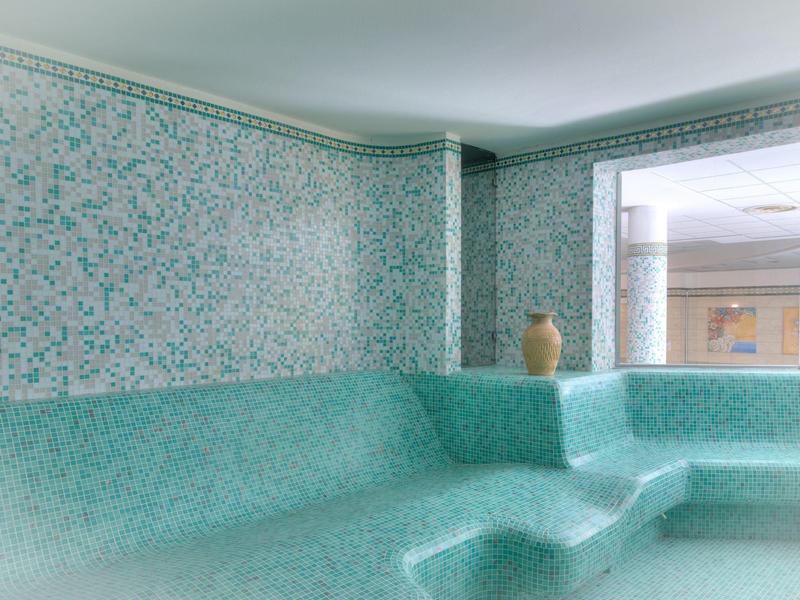 Idromassaggio azzurro chiaro con piastrelle decorate e grande vaso nell'area benessere.