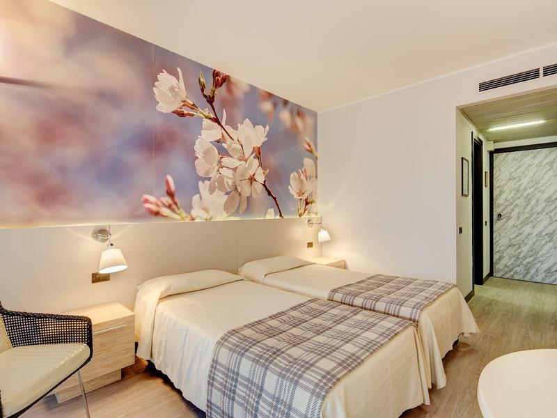 Camera d'hotel luminosa con due letti e un grande dipinto floreale sulla parete.