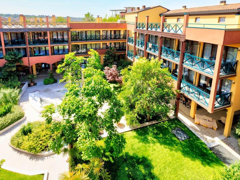Cortile di un hotel con giardini verdi e balconi in una giornata di sole.