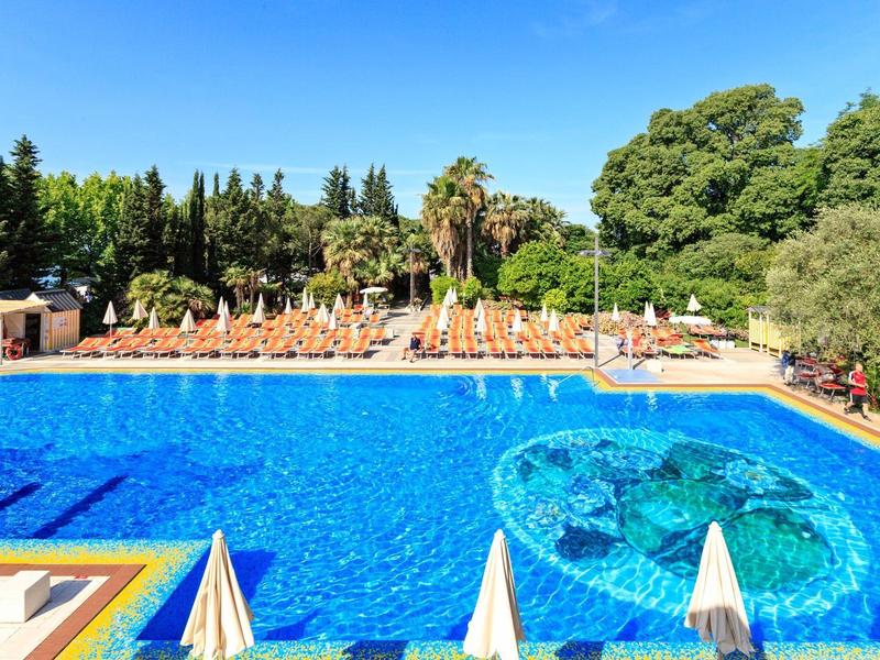 Grande piscina all'aperto con superficie d'acqua blu e lettini lungo il bordo sotto un cielo azzurro.