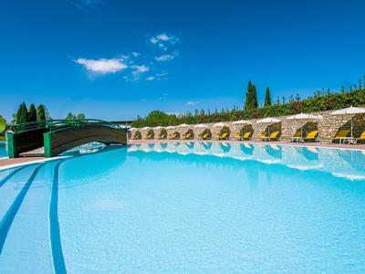 Grande piscina dell'hotel con acqua limpida e blu e un ponte sullo sfondo sotto un cielo azzurro.