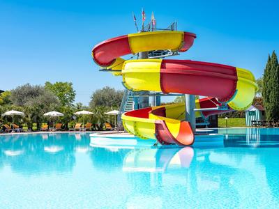 Grande scivolo d'acqua colorato in piscina con ombrelloni sullo sfondo.