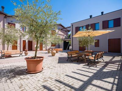 Cortile di un hotel con zona pranzo, ombrellone e piante in vaso sotto un cielo limpido.