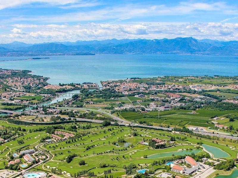 Luchtfoto van een groen vakantieoord met golfbanen aan zee en bergen op de achtergrond.