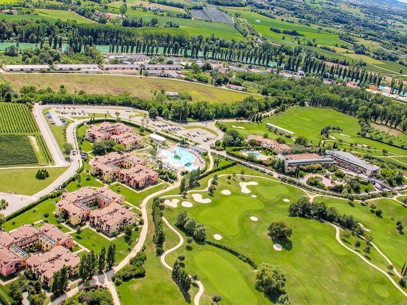 Luchtfoto van een resort met meerdere gebouwen, een zwembad en uitgestrekte groene gebieden.