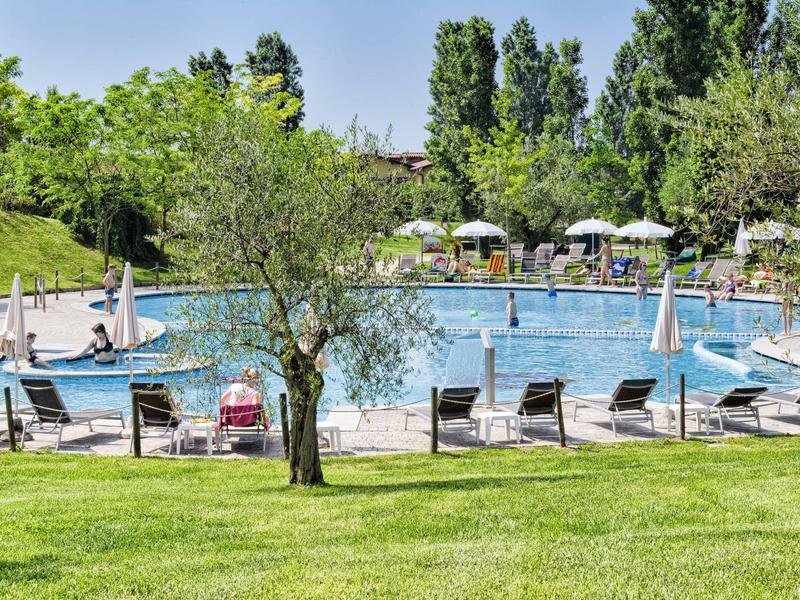 Groot buitenzwembad met ligstoelen en parasols in een groene hotelomgeving bij zonnig weer.