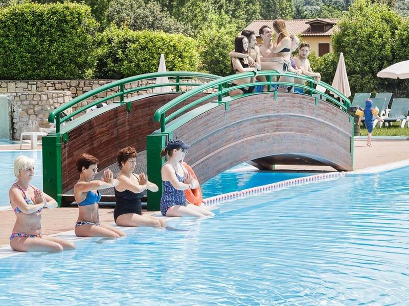Vijf vrouwen zitten aan de rand van een zwembad met ontspannen sfeer en brug op de achtergrond.
