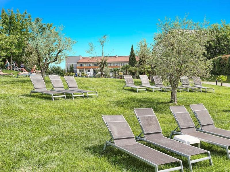 Groen grasveld met verspreide ligstoelen en gebouwen op de achtergrond op een zonnige dag.