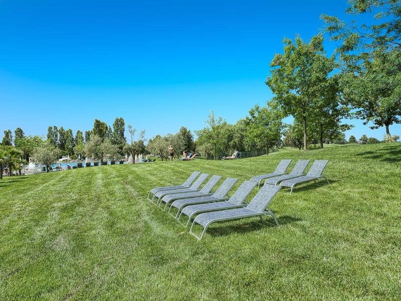 Lege ligstoelen op goed onderhouden gras onder een blauwe lucht in een buitenruimte van een hotel.