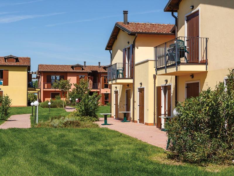 Moderne vakantiewoningen met balkons en goed onderhouden tuin onder een heldere hemel.