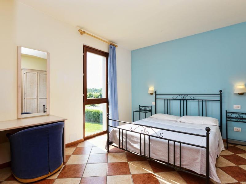 Lichte hotelkamer met tweepersoonsbed, blauwe accentmuur, betegelde vloer en toegang tot balkon of tuin.