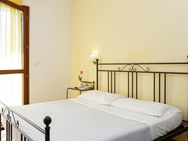 Lichte slaapkamer met metalen bed, nachtkastje en lamp naast een balkondeur.