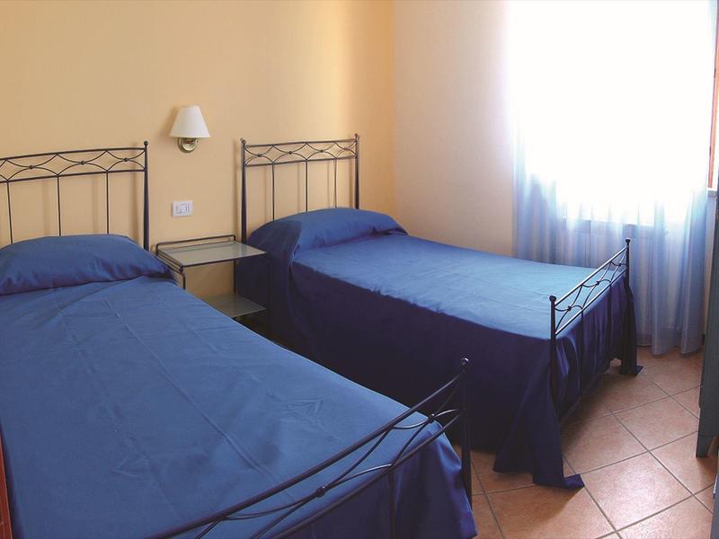 Twee eenpersoonsbedden met blauwe dekens in een eenvoudig ingericht hotelkamer met gele muren.