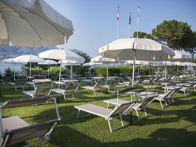 Sonnenliegen und weiße Sonnenschirme stehen geordnet auf einer grünen Wiese bei klarem Himmel.