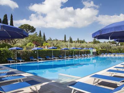 Freier Pool mit blauen Liegestühlen und Sonnenschirmen, umgeben von grüner Vegetation und blauem Himmel.