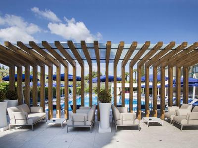 Moderne Terrasse mit Holzpergola, mehreren weißen Sesseln und großen Pflanzkübeln vor blauem Himmel.