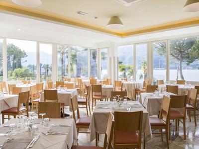 Helles Restaurant mit großen Fenstern, Holzmöbeln und gedeckten Tischen mit weißen Tischdecken.