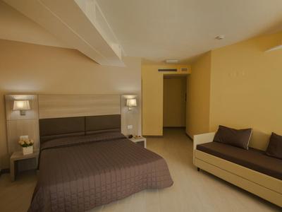 Ein schlichtes Schlafzimmer mit beigem Farbton, einem Doppelbett und einem braunen Sofa.