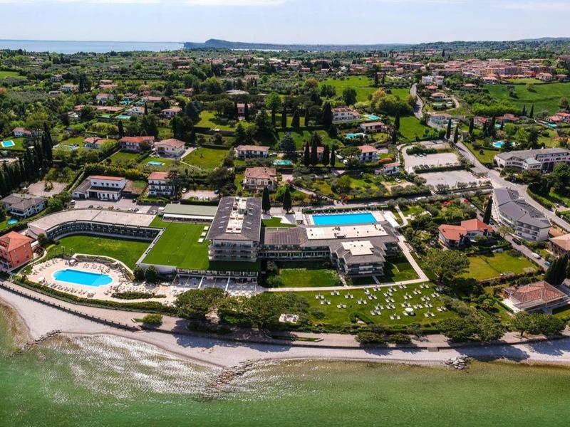 Küstenresort mit grünen Gärten, mehreren Pools und Sandstrand entlang des klaren blauen Meers.