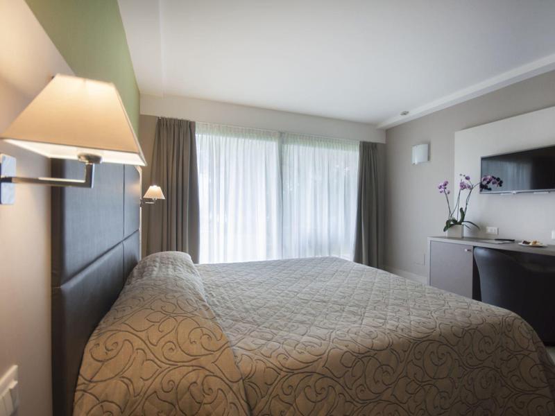 Modern eingerichtetes Schlafzimmer mit großem Bett, Panoramafenster und Flachbildschirm an der Wand.