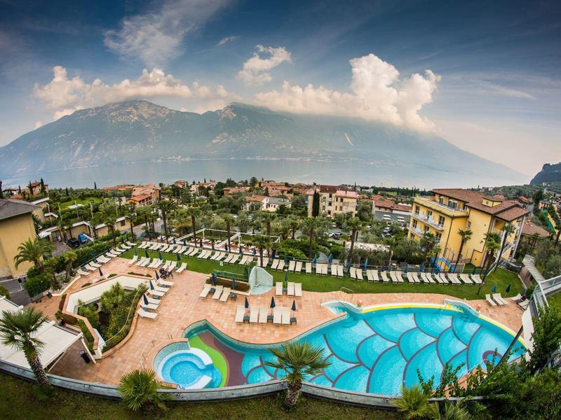 Hotel pool with sun loungers and mountain view under cloudy sky.