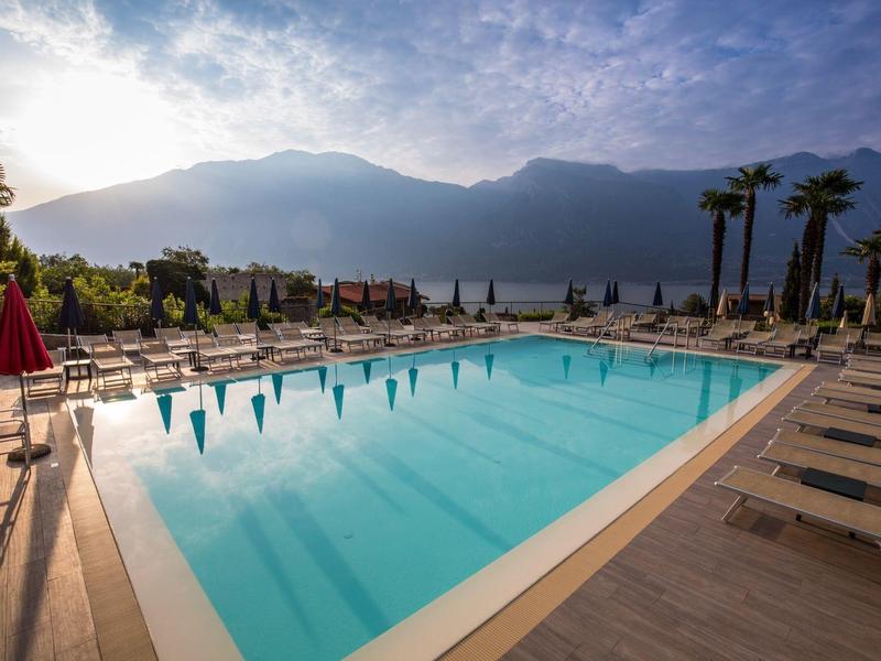 A large pool with lounge chairs and palm trees, mountains visible in the background under a cloudy sky.
