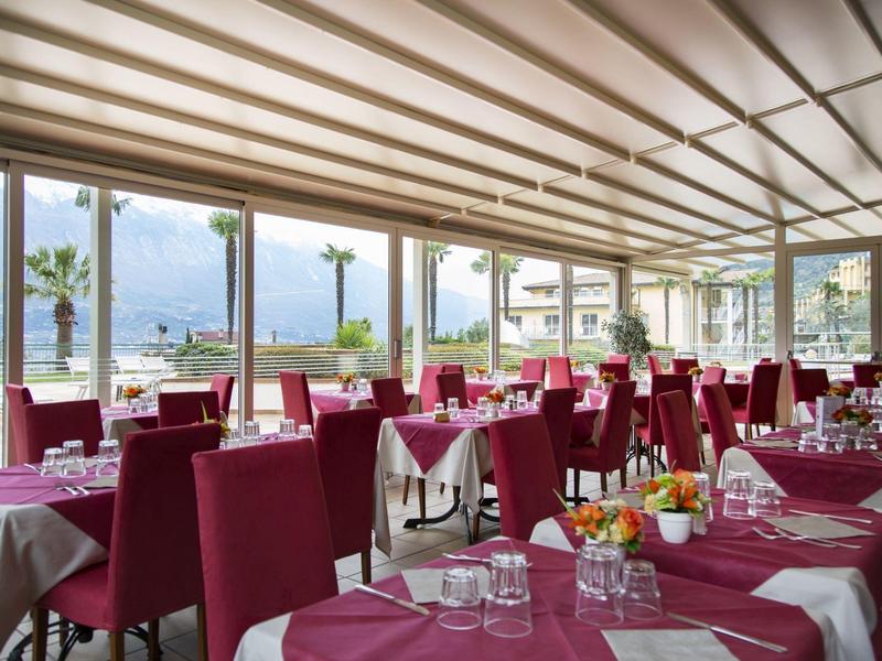 Large dining room with tables covered in red tablecloths and large windows overlooking the sea.