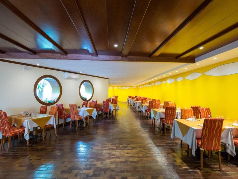 Large dining room with yellow walls, wooden floor, and round windows.
