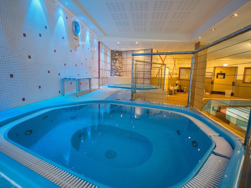 Indoor pool with hot tub, changing rooms, and modern lighting in a hotel area.