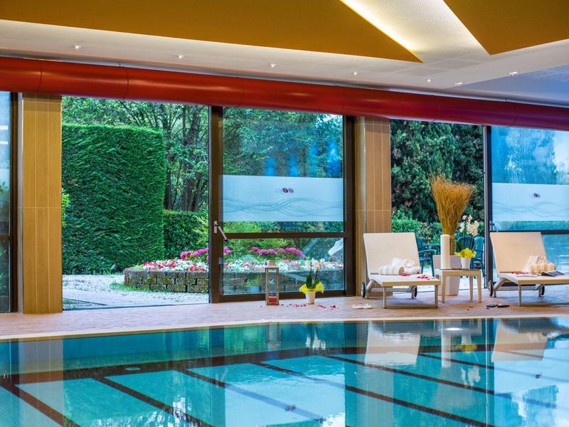 Indoor pool with lounge chairs and garden view through large windows.