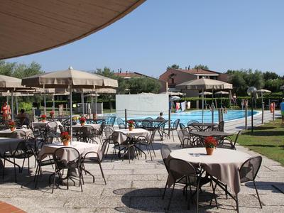 Outdoor restaurant with set tables next to a pool and pavilions under clear sky.