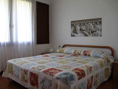 Simple bedroom with large bed, patterned bedspread, window, and wall art.