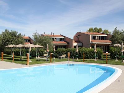 Mehrere Ferienhäuser mit Blick auf einen großen Pool unter blauem Himmel.