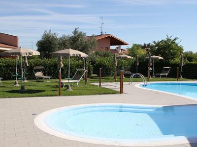 Swimming pool with lounge chairs and umbrellas in a well-kept garden under clear sky.