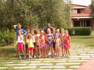 Group of people in swimwear standing on paved pathway in front of building with trees in background.