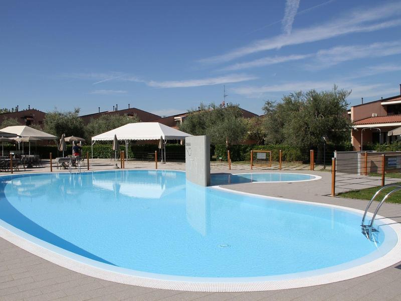 Clear outdoor swimming pool with sun umbrellas and garden surrounded by residential buildings.