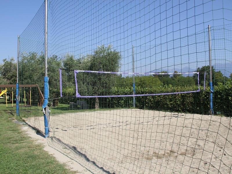 Outdoor sand volleyball court with net and fencing on grassy area