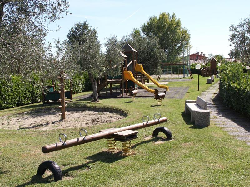 Playground with seesaw, sandbox, slide, and trees in a green garden area