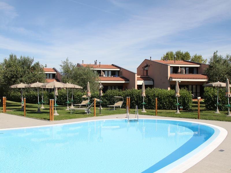 Residential houses with red roofs behind a clear outdoor pool and green garden under blue sky.