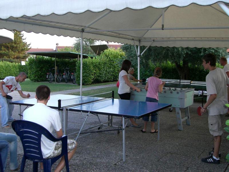 People playing table tennis and foosball under an outdoor canopy.