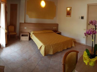 Habitación de hotel con cama doble, mesa de noche, silla y orquídea floreciendo sobre la mesa