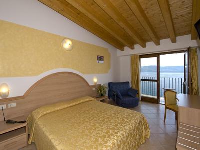 Habitación de hotel con cama doble, sillones y balcón con vista al mar bajo vigas de madera.