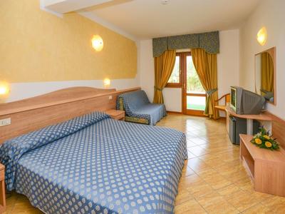 Acogedora habitación de hotel con cama doble, sillón, TV y balcón con cortinas.