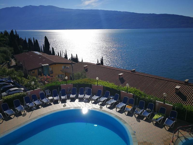 Piscina con tumbonas junto a un lago y montañas al fondo con cielo despejado.