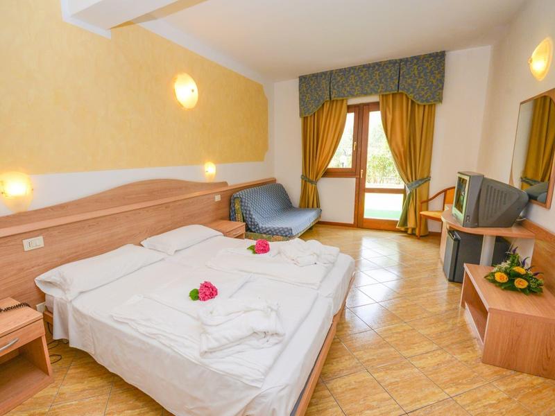 Habitación de hotel luminosa con cama doble, sillones, escritorio y balcón con vista verde.