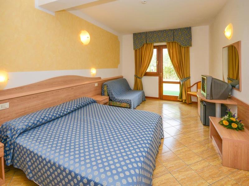 Acogedora habitación de hotel con cama doble, sillón, TV y balcón con cortinas.