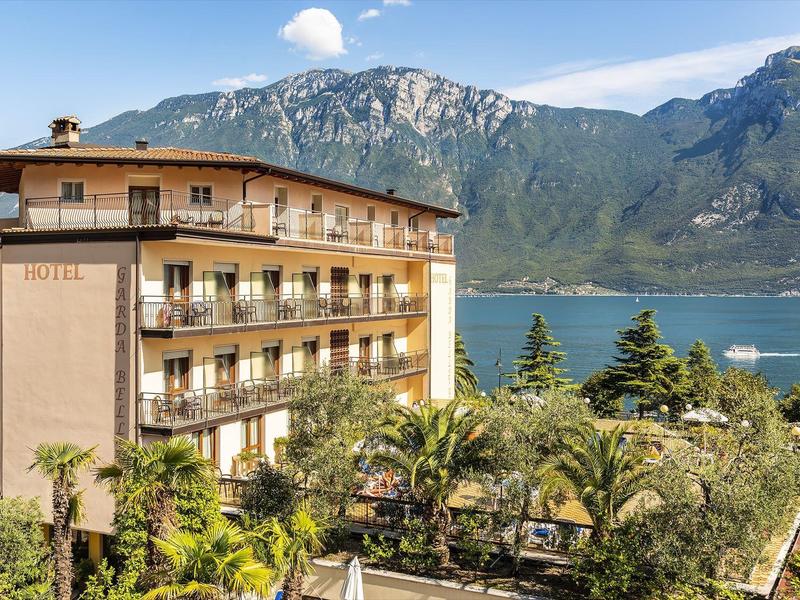 Hotel u jezera s horami v pozadí a palmami v popředí.