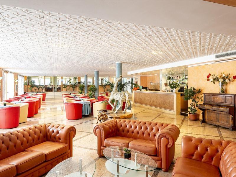 Světlá, útulná hotelová hala s hnědými koženými pohovkami a červenými křesly.